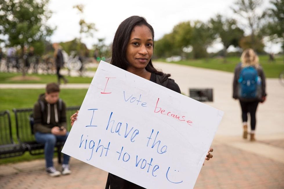 Student holding a sign reading "I vote because I have the right to vote."